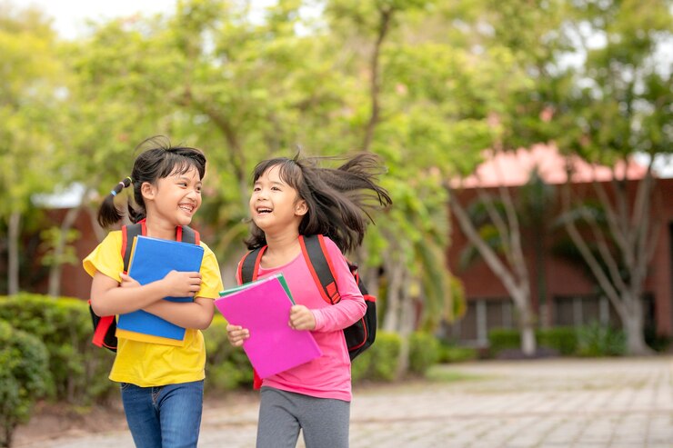 Photo 学校に戻る。本を持ってランドセルを持って学校で一緒に歩く2人のかわいいアジアの子供女の子