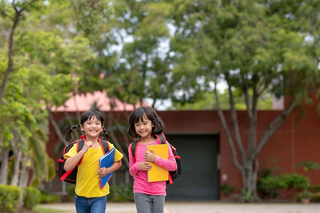 Back to school. Two cute asian child girls with school bag holding book and walk together in the school