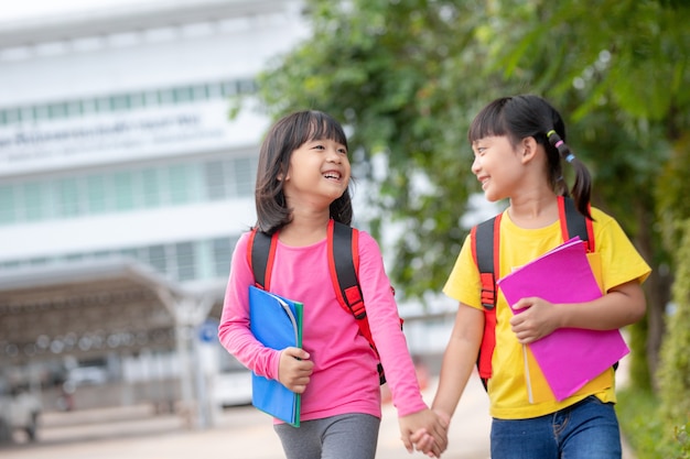 Photo back to school. two cute asian child girls with school bag holding book and walk together in the school