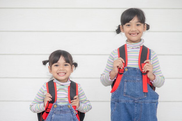 학교로 돌아온 두 명의 귀여운 아시아 어린이 소녀가  바탕에 책을 들고 학교 가방을 들고 있습니다.