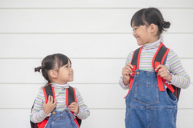 Back to school Two cute Asian child girls with school bags together on white background