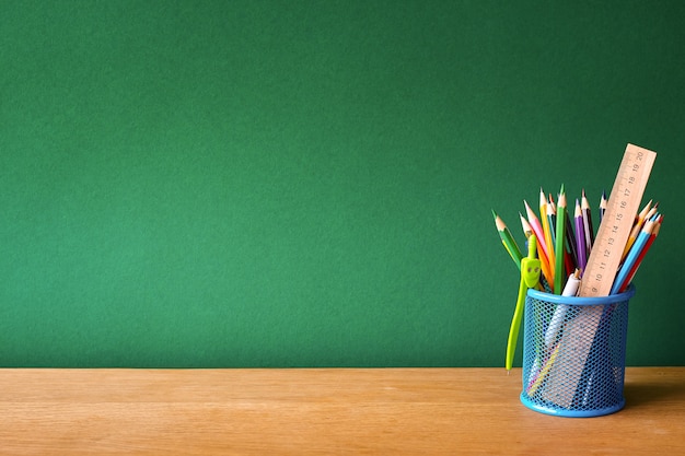 Photo back to school with blue glass with school supplies on a school desk on a background of a clean green chalk board