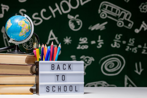 Photo back to school with books, pencils and globe on white table on a green blackboard