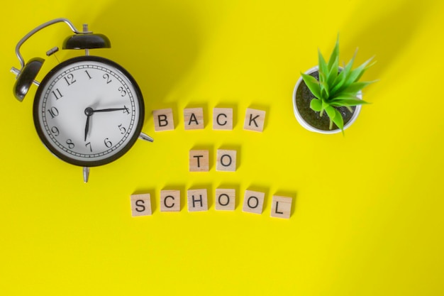 Back to schoolwooden letters and an alarm clock on a yellow background top view