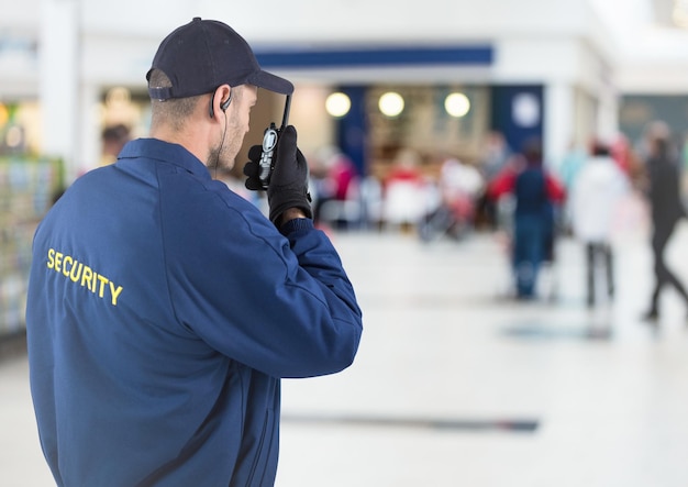 Photo back of security guard with walkie talkie against blurry shopping centre