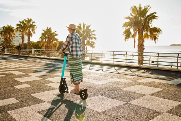 写真 背中のシニア女性と電動スクーターで旅行 夏休みと通勤 休憩でリラックスして旅行 成熟した女性の高齢者の女性または環境に優しい交通手段での旅行 サステナブルで休日