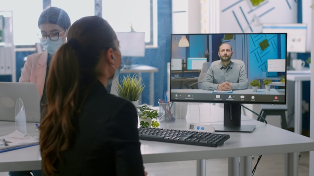 Back shot of businesswoman wearing medical face mask talking on videocall meeting with remotely team. Executive freelancer working in new normal company office during coronavirus pandemic