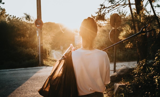 Immagine posteriore della donna che tiene un sacco della spazzatura e un raccoglitore di rifiuti mentre pulisce la foresta