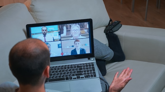 Back shot of tired man lying on sofa while chatting with teammates