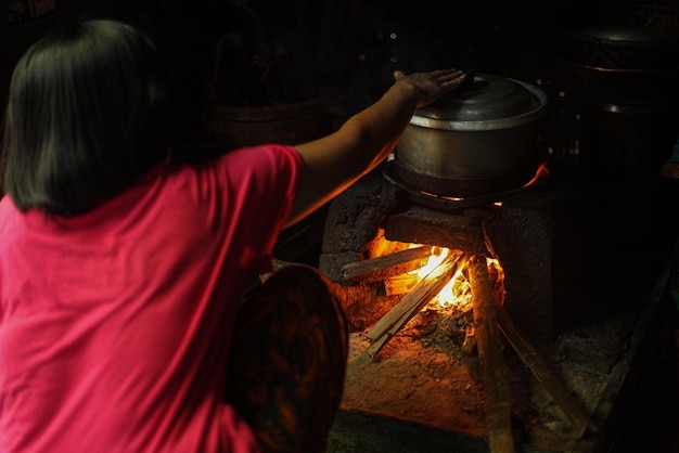 薪のキュービクルキットで燃やされた薪で伝統的なストーブで調理するアジアの地元の女性の裏側
