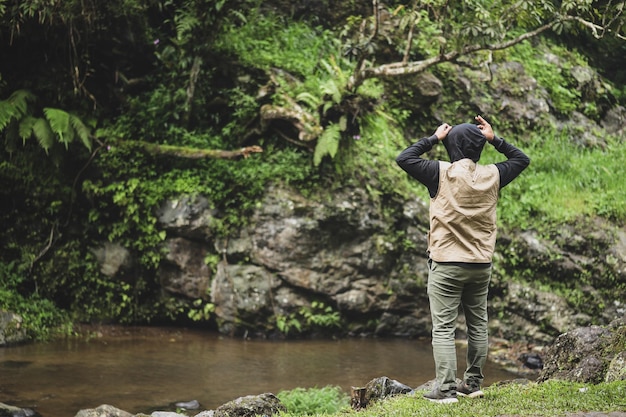 Back side of Asian man in casual style wearing hoodie and enjoying view of river village and green f