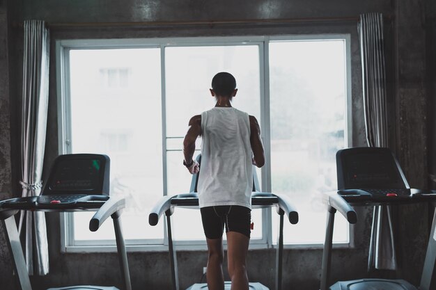 Back side of asian sportman runner running on treadmill in fitness club Cardio workout Healthy lifestyle guy training in gym Sport running concept