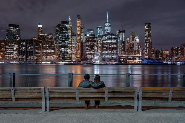 Back side couple sitting and looking new york cityscape beside the east river at the night time
