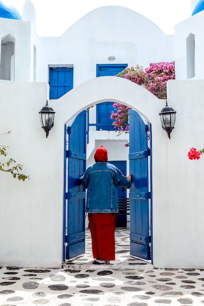 무슬림 여성의 뒷면은 산토리니에서 전통적인 그리스 집의 문을 엽니 다