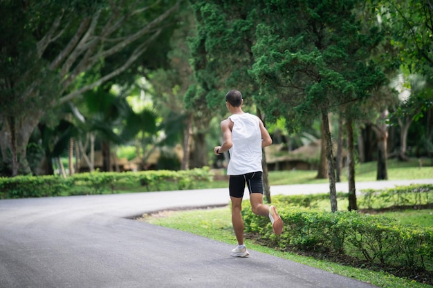 背面図アジア人のスポーツマンは、庭で走ったりジョギングをしたりしながらスマートウォッチを身に着けている体にフィットし、公園で運動する木ときれいな空気を持っていますスポーツの健康的なランニングのコンセプト