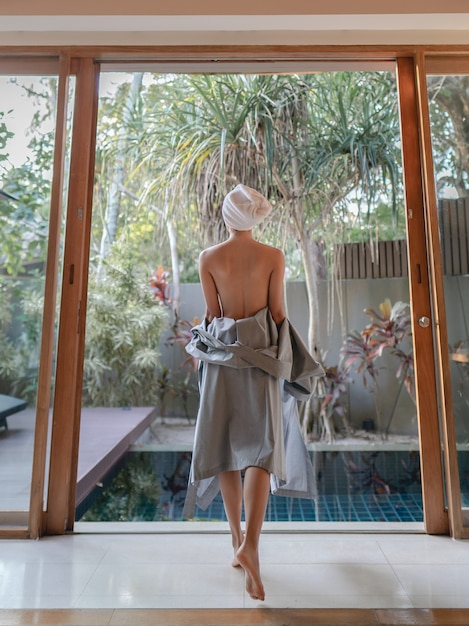 Back side of woman taking off bathrobe and walking to the pool.