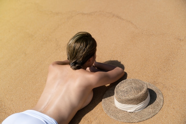 Back side woman topless lying down on sand beach relaxing sunbathing.