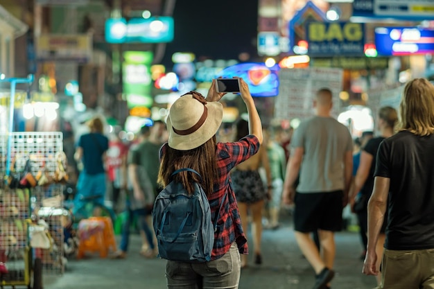 카오산 로드 워킹 스트리트에서 사진을 찍는 젊은 아시아 여성의 뒷면