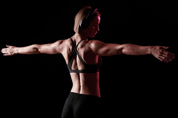 Dietro di una sportiva con un corpo muscoloso che si allunga dopo l'allenamento, la ragazza magra ascolta musica durante l'allenamento