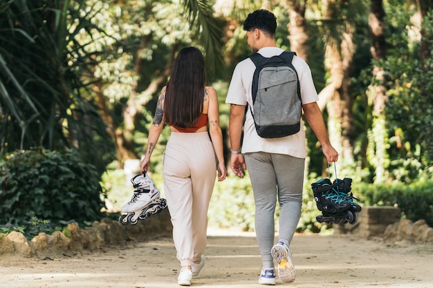 Back of two young people walking in a park carrying inline skates