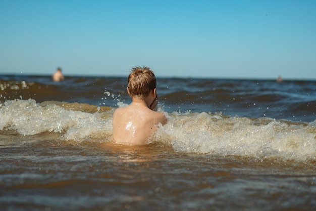 Back view of 7-8 years old cute caucasian boy swim in the sea with big splashes. Child enjoys swimming in the ocean. Holidays, vacation with kids