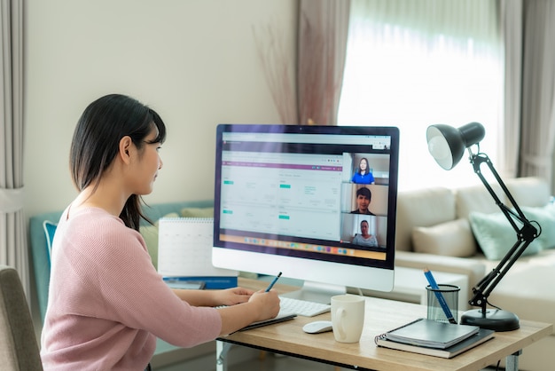 Punto di vista posteriore della donna asiatica di affari che parla con suoi colleghi del piano nella videoconferenza.