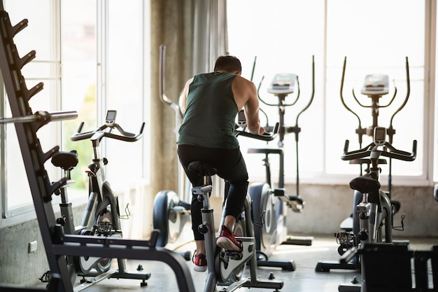 Photo back view asian sportsman exercising on a bicycle in the gym determination to cardio lose weight makes her healthy exercise bike man fitness sport concept