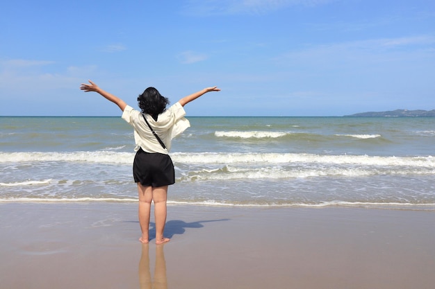 Il punto di vista posteriore della donna asiatica alza le mani con il cielo del mare e le nuvole bianche natura e donna potente