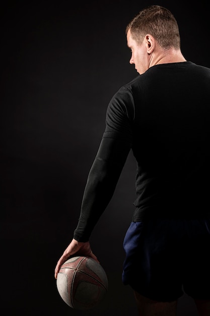 Back view of athletic male rugby player holding ball with copy space