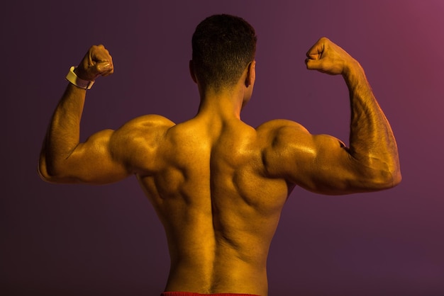 紫色の背景に上腕二頭筋を示す筋肉の胴体を持つ運動男性の背面図