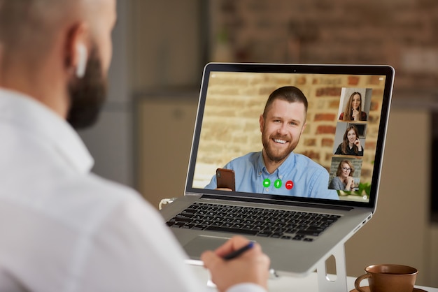 Photo back view of a bald male employee in earphones who is doing notes during a video conference.