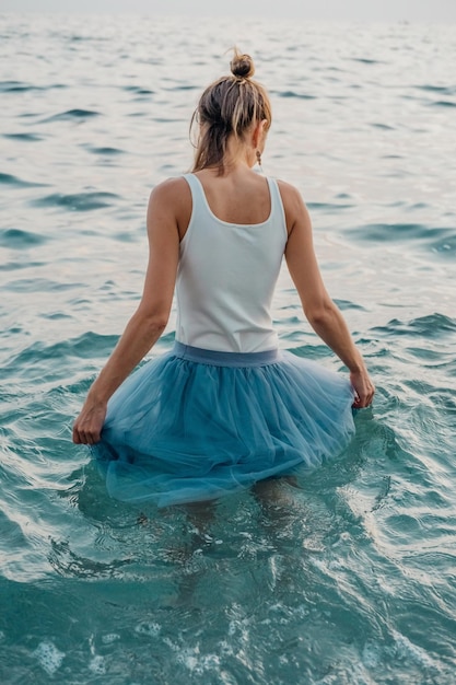 Back view of beautiful girl posing in sea waves in evening fashion photoshoot