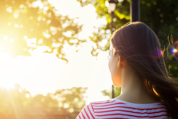 Punto di vista posteriore di bella ragazza romantica che legge un libro nel parco