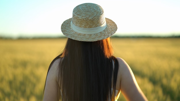 写真 緑の野原を歩く帽子と美しい若い女性を背面します。