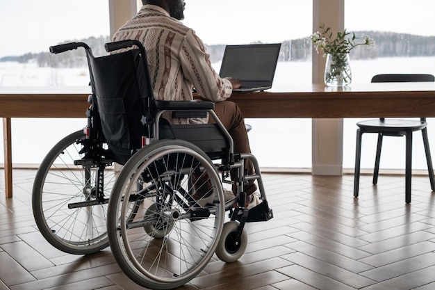 Back view of black man in casualwear typing on laptop keyboard at home