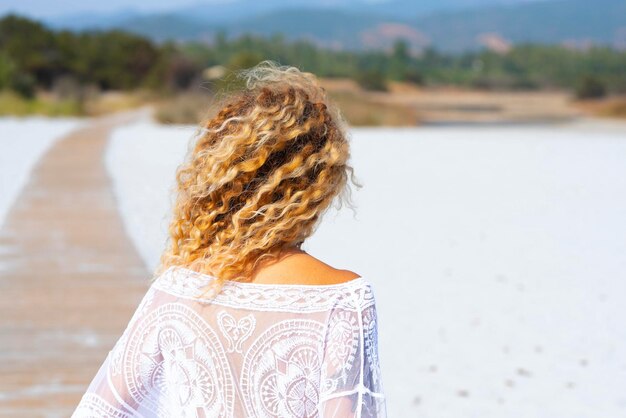 Back view of blonde surf waves hairstyle woman enjoying the beach in summer holiday vacation Concept of tourist and tourism in the nature Female people walking on the sand outdoor