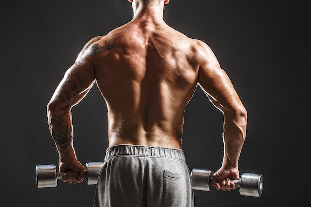 Back view of bodybuilder training with dumbbell isolated on black