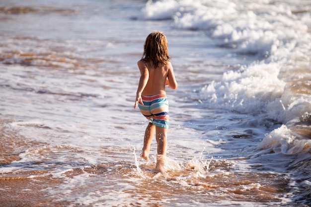 Back view of boy running beach near the seaside Excited amazed kid having fun with running through water in ocean or sea