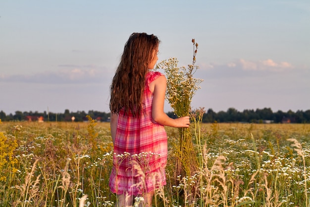 Back view brunette girl in the red dress holds bouquet of flowers. Romantic evening sky.