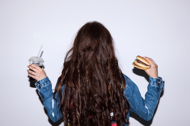 Vista posteriore della donna bruna con fast food che tiene in mano stile di vita malsano delle persone e concetto di cibo spazzatura