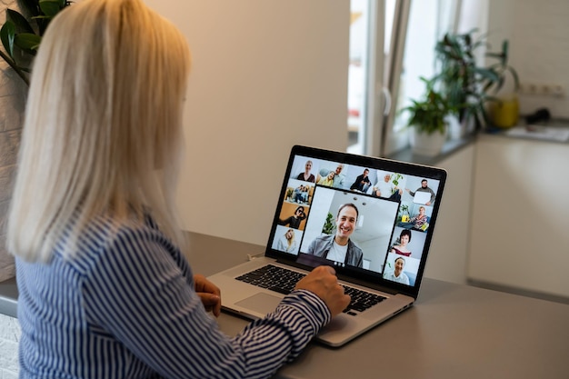 Foto vista posteriore della donna d'affari che parla con i suoi colleghi del piano in videoconferenza. team aziendale multietnico che utilizza laptop per una riunione online in videochiamata. gruppo di persone che lavorano in smart working da casa