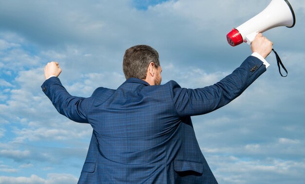 Back view of businessman hold megaphone on sky background