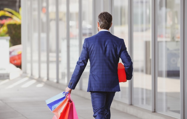 Back view of businessman holding shopping bags and walking in shopping store