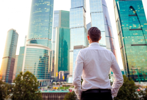 Back view of businessman looking on copy space while standing against glass skyscraper