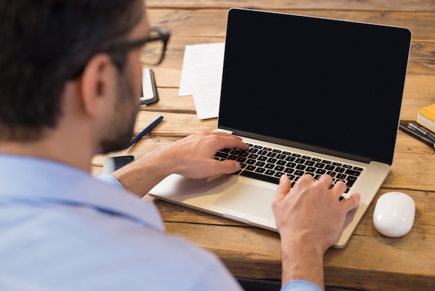 Vista posteriore dell'uomo d'affari seduto davanti allo schermo del laptop. uomo che digita su un moderno laptop in un ufficio. giovane studente che scrive sul computer che si siede al tavolo di legno.