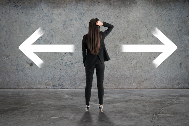 Back view of businesswoman with two arrows in concrete interior Different direction and choice concept