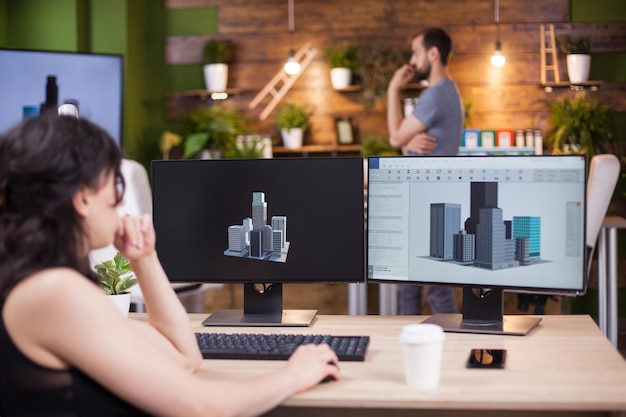 Вид сзади деловой женщины, сидящей за столом в офисе и работающей над своим проектом. Молодой сотрудник в фоновом режиме работает.