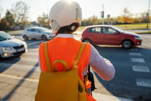 Photo back view of a careful young woman in vest and helmet on electric scooter in traffic