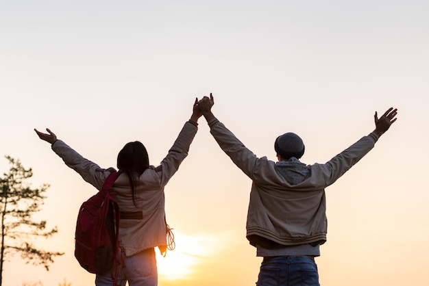 Back view of the caucasian couple holding hands of each other and looking at the sunset. Traveling concept