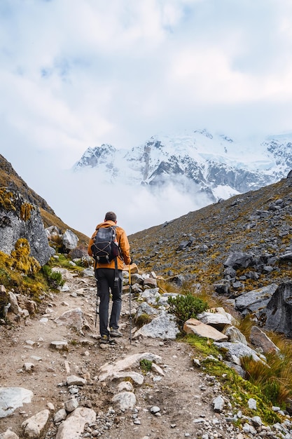 Вид сзади на кавказца, идущего в гору на вершину в заснеженном горном ландшафте